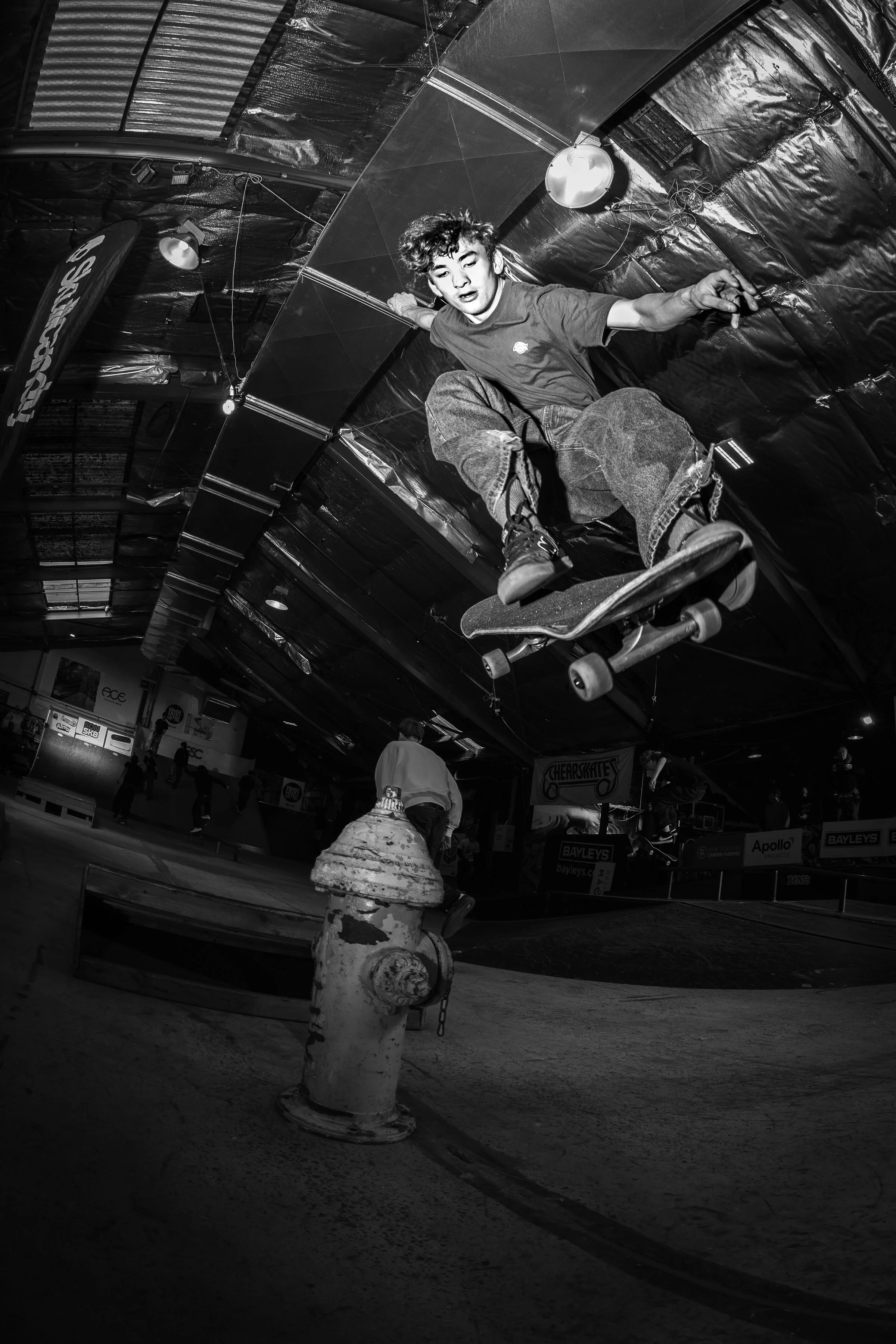 Black and white image of a skateboarder performing an aerial trick over a fire hydrant in an indoor skate park.